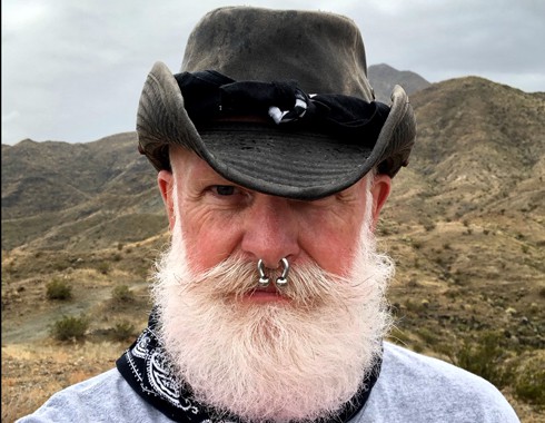 Vintage black felt hat with band and scenic desert background, featuring a bearded man with septum piercing.