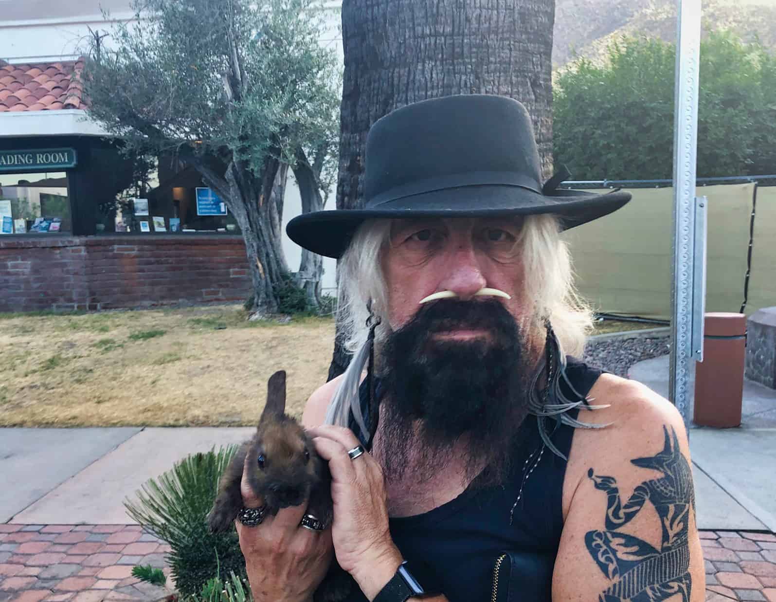 Distressed biker with tattoo holding a bunny outside, urban setting, expressive pose.