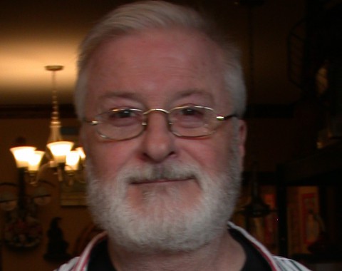 Close-up of smiling man with white hair and beard in cozy indoor setting.