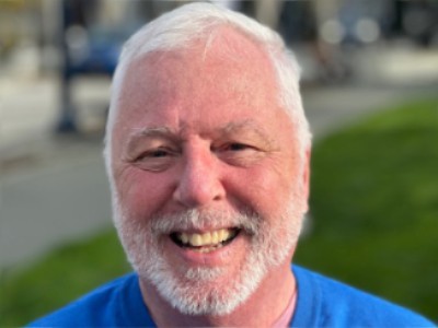 Close-up of a smiling man with white hair and beard outdoors, promoting Rattling Good Yarns.