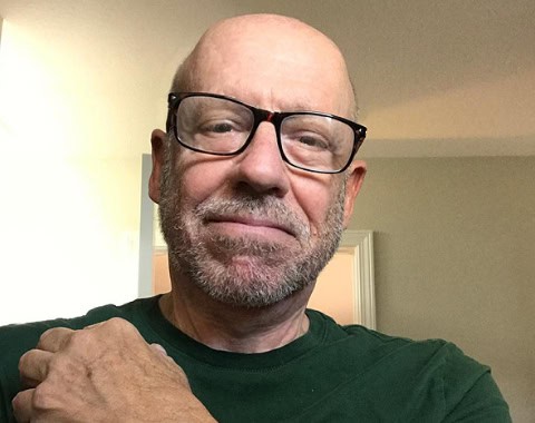 Prominent man wearing glasses and green shirt, smiling confidently in indoor setting.