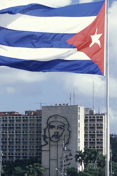 Cuban flag flying over modern buildings. The face of Che Guevara is on the side of the building.