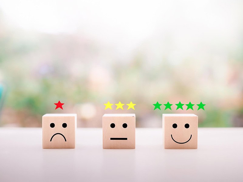 Three blocks with simple faces on them with tow dots for eyes and lines for mouths. The three blocks are showing different emotions, unhappiness, no reaction and smiling.