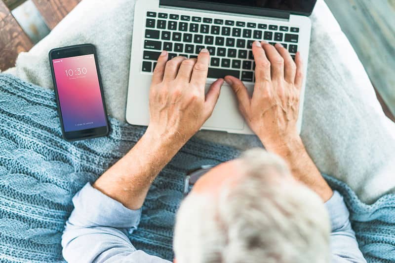 Senior person using laptop and smartphone.