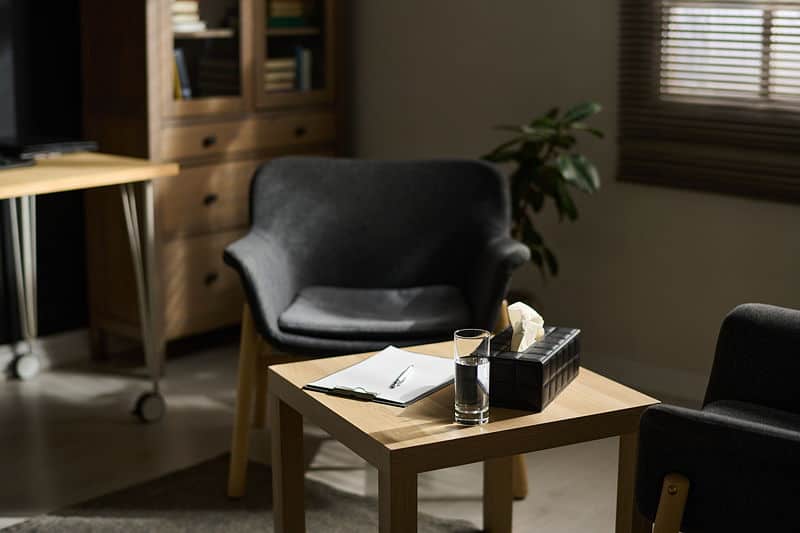 Calm therapy office with two empty armchairs facing a small table holding a glass of water, tissues, and a clipboard, ready for a counseling session.